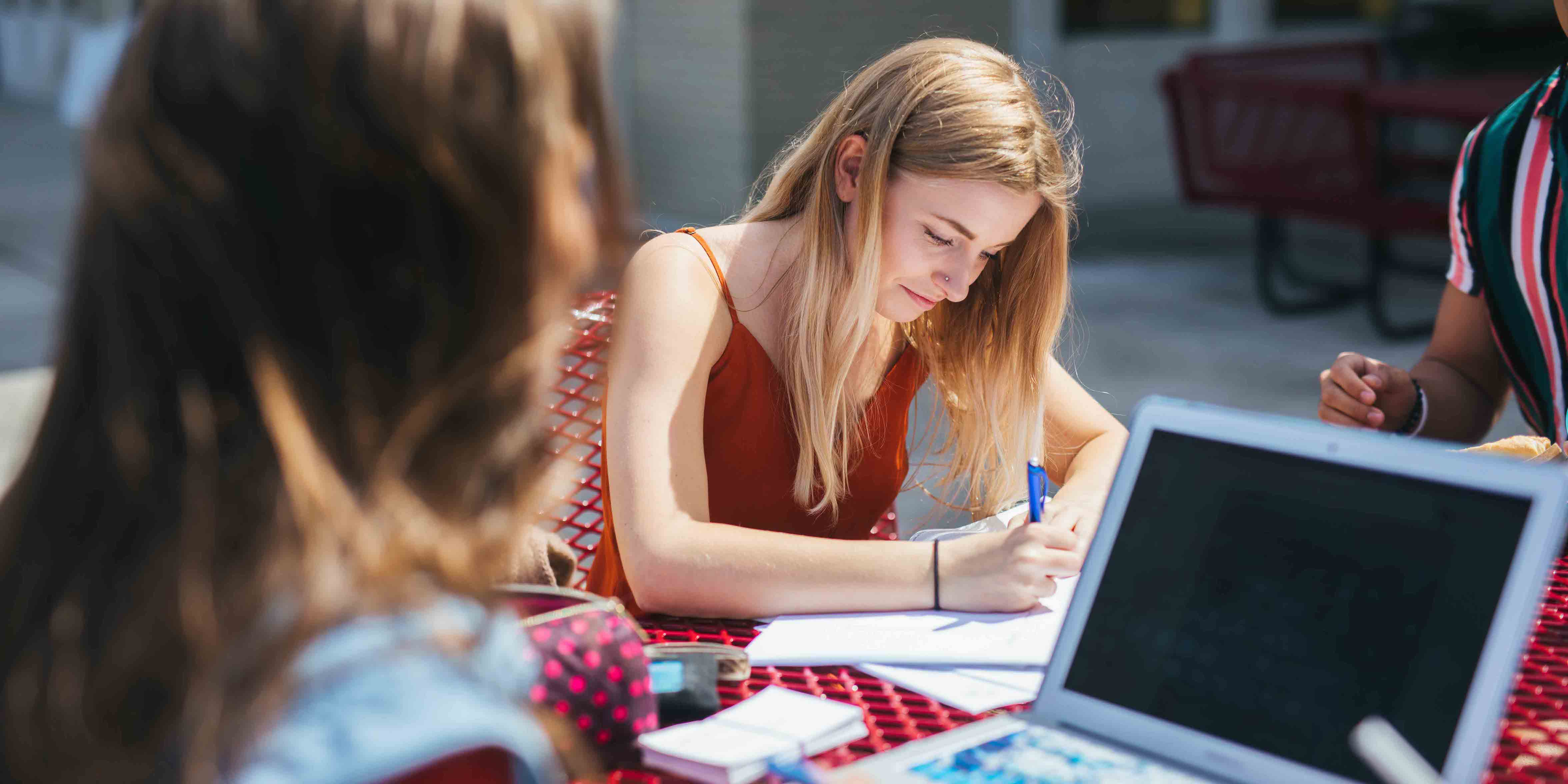 female students sitting at outdoor table writing homework