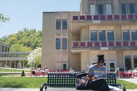 Woman doing homework on a bench on campus