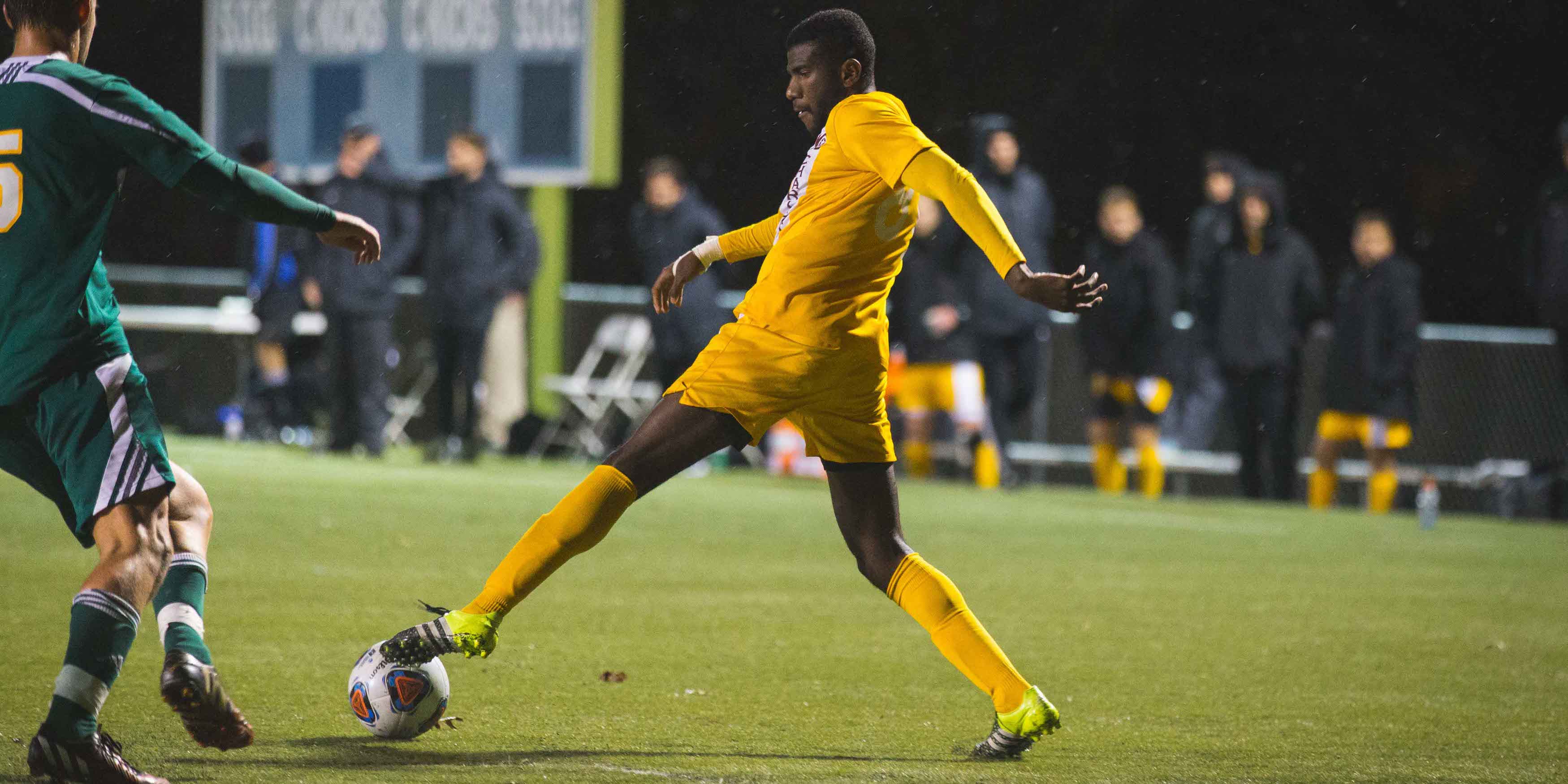 male soccer player blocking opposing team from kicking soccer ball on soccer field