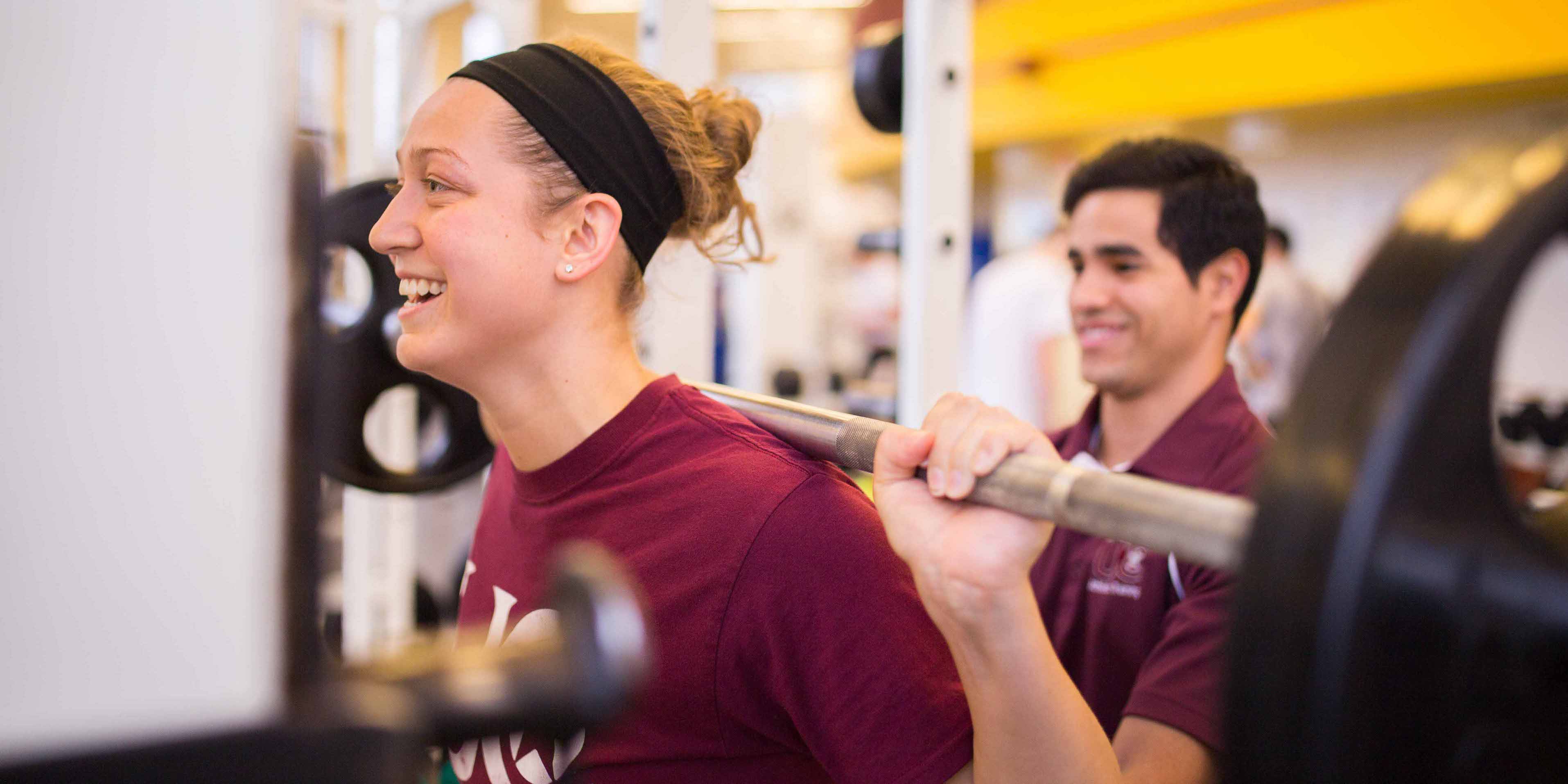 female student lifting weights with male spotter