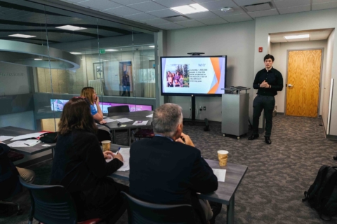 male student presenting a powerpoint slide to business professionals in a classroom