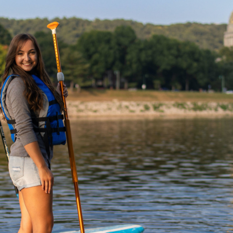 male and female student posing on paddle boards in river with Capitol in background