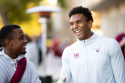 Two male students laughing while wearing athletic apparel