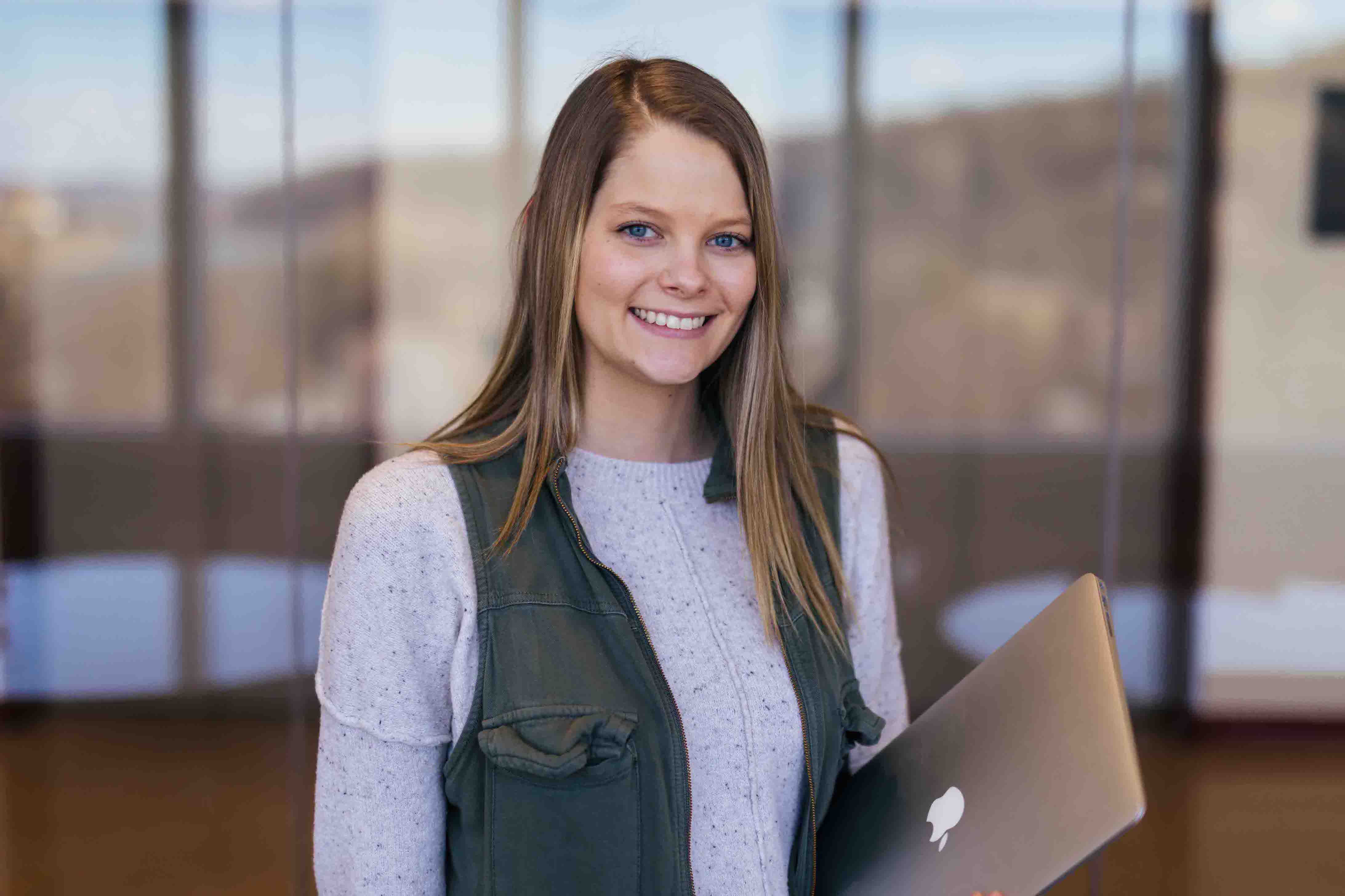 female student smiling at camera while holding laptop