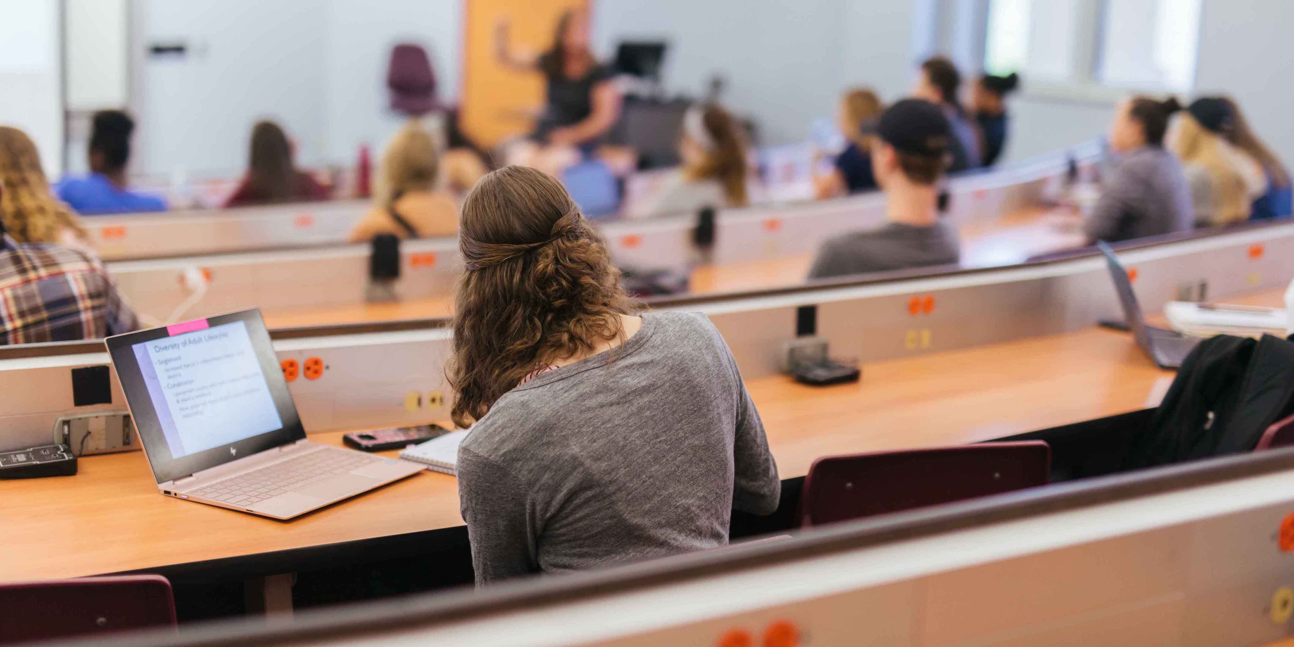back view of female student taking notes during class lecture