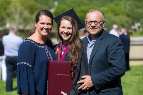 female graduate in cap and gown posing with family