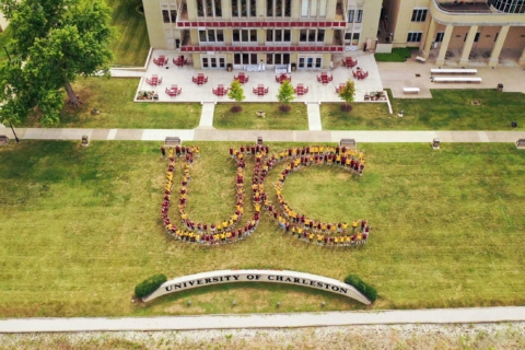 UC students standing together to create a U and a C outline on the riverbank lawn