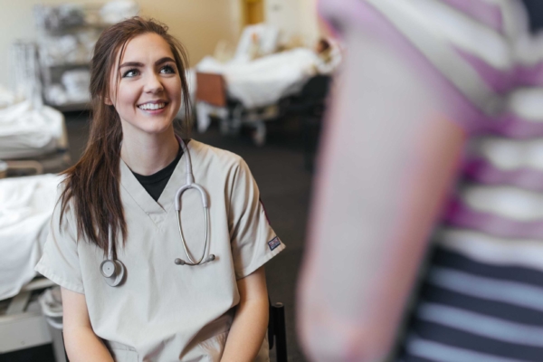 Nursing student in scrubs listening to mock patient