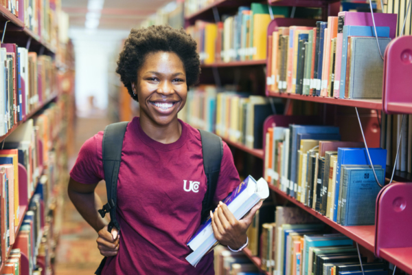 smiling student with backpack and books in the library stacks