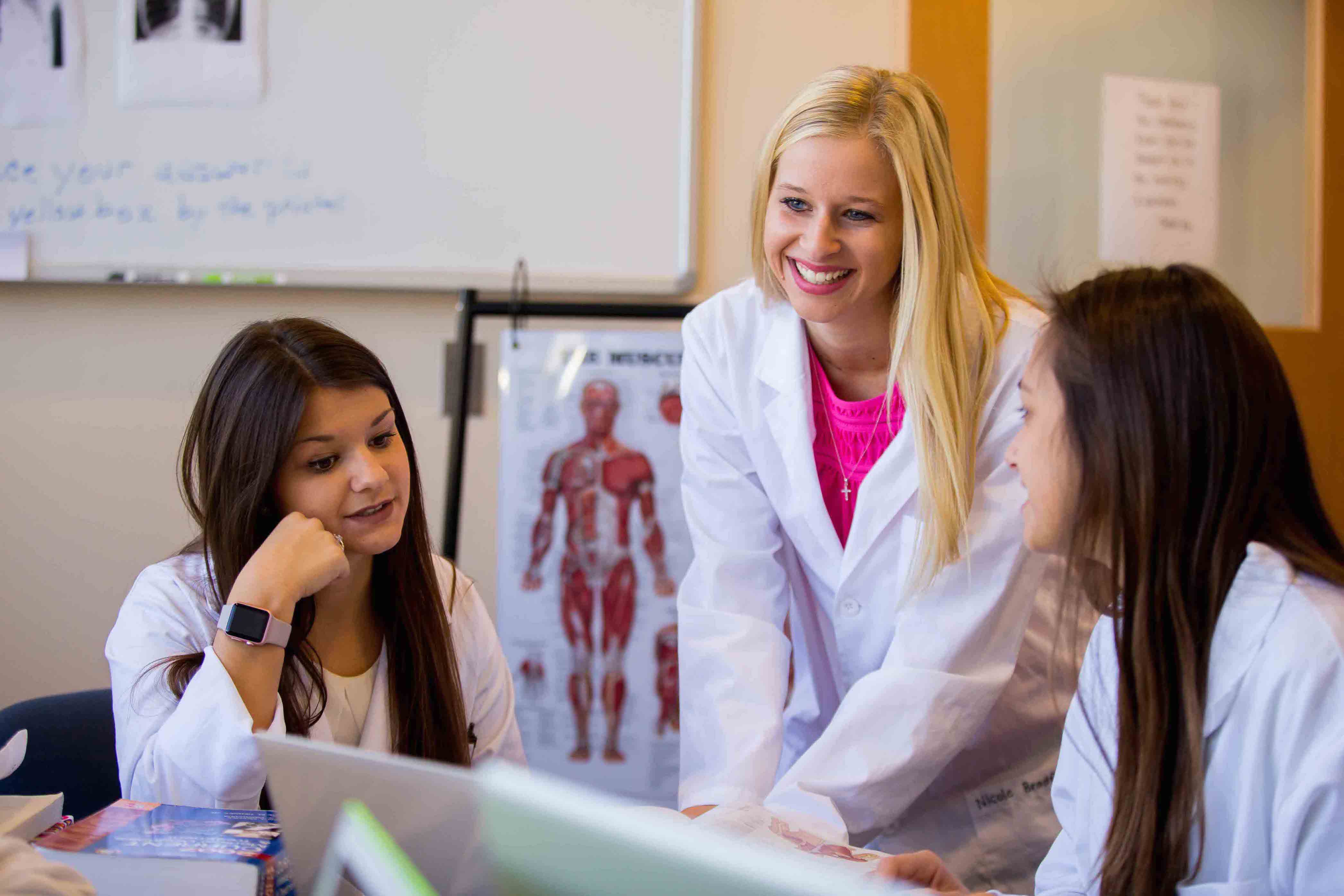 three female students in lab coats working on a laptop