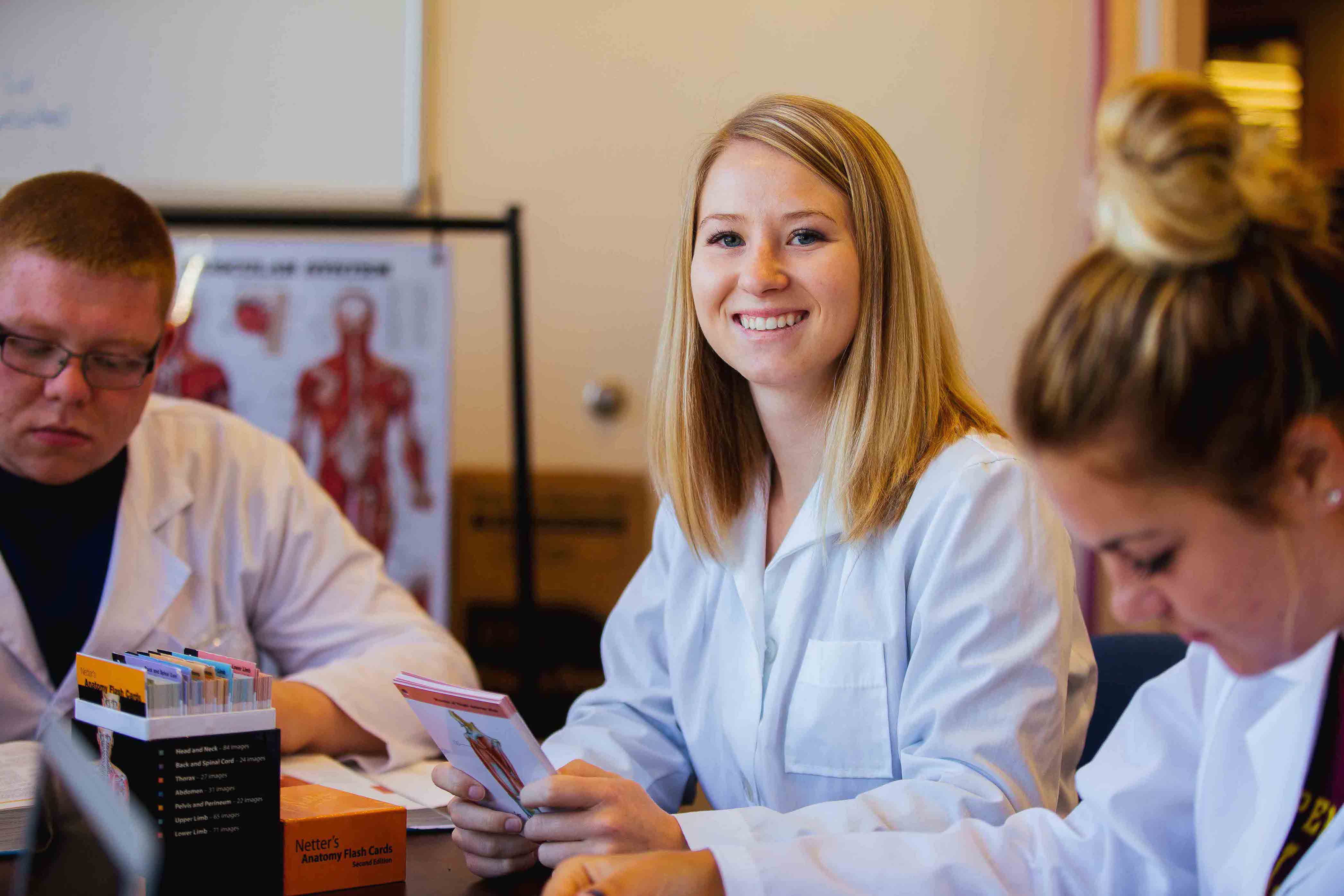 smiling female student in lab coat holding anatomy flash cards