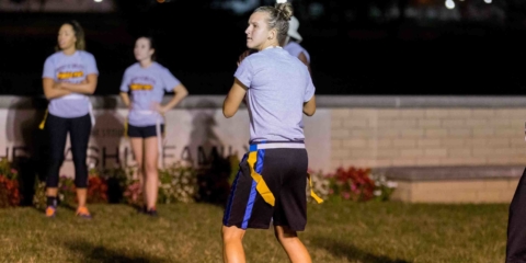 Students playing flag football on the riverbank lawn