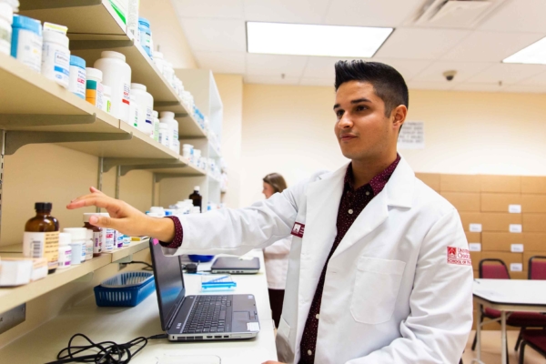 Student Pharmacist reaching for medicine bottle of shelf