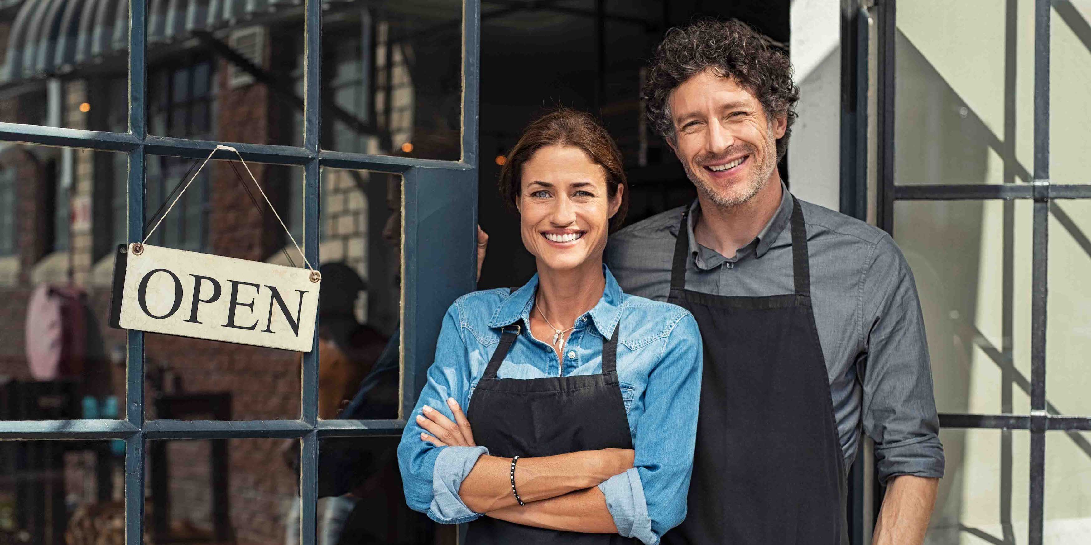 Two cheerful small business owners smiling and looking at camera while standing at entrance door.