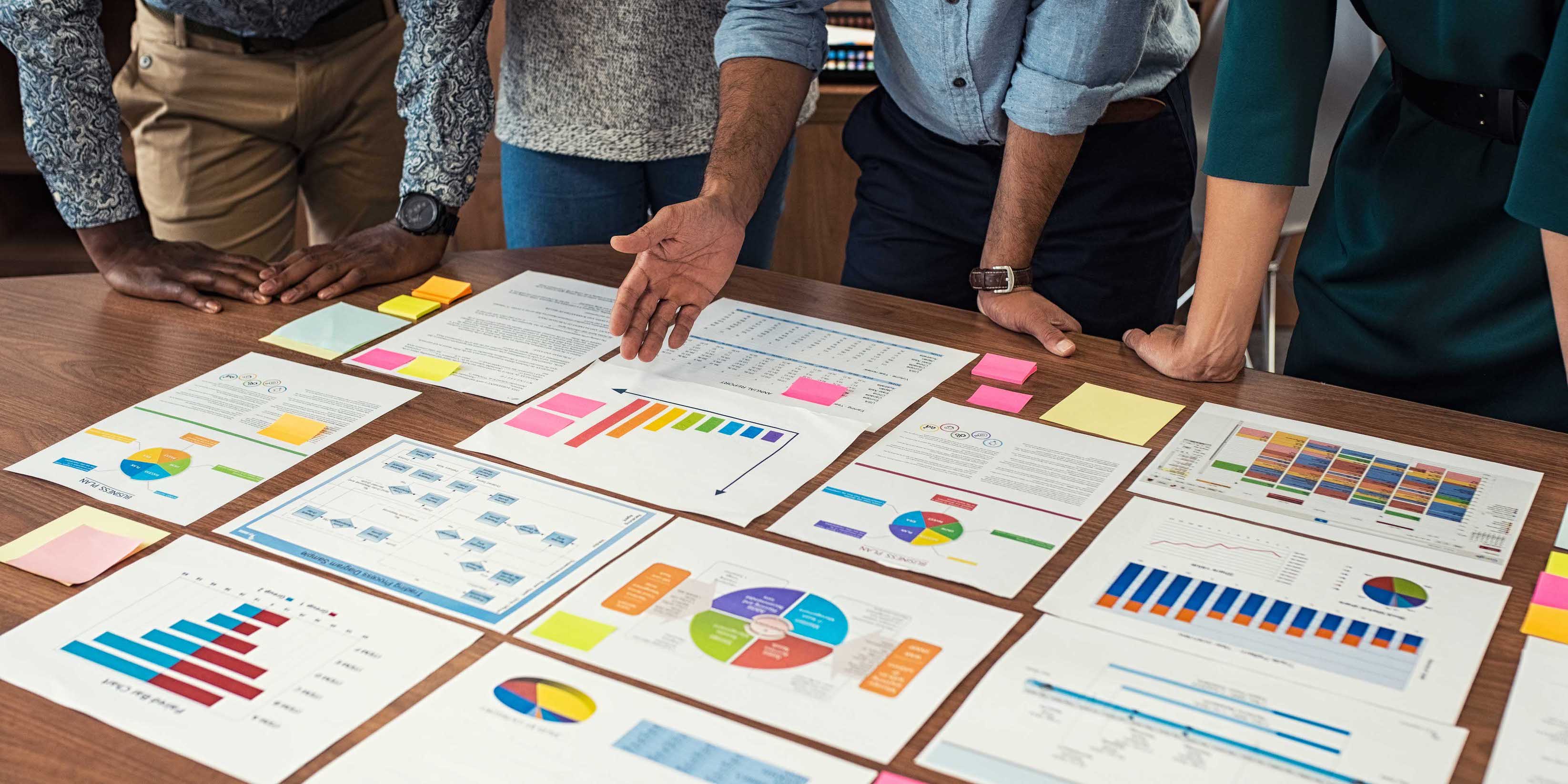 Financial and business documents on table with multiple hands working on it.