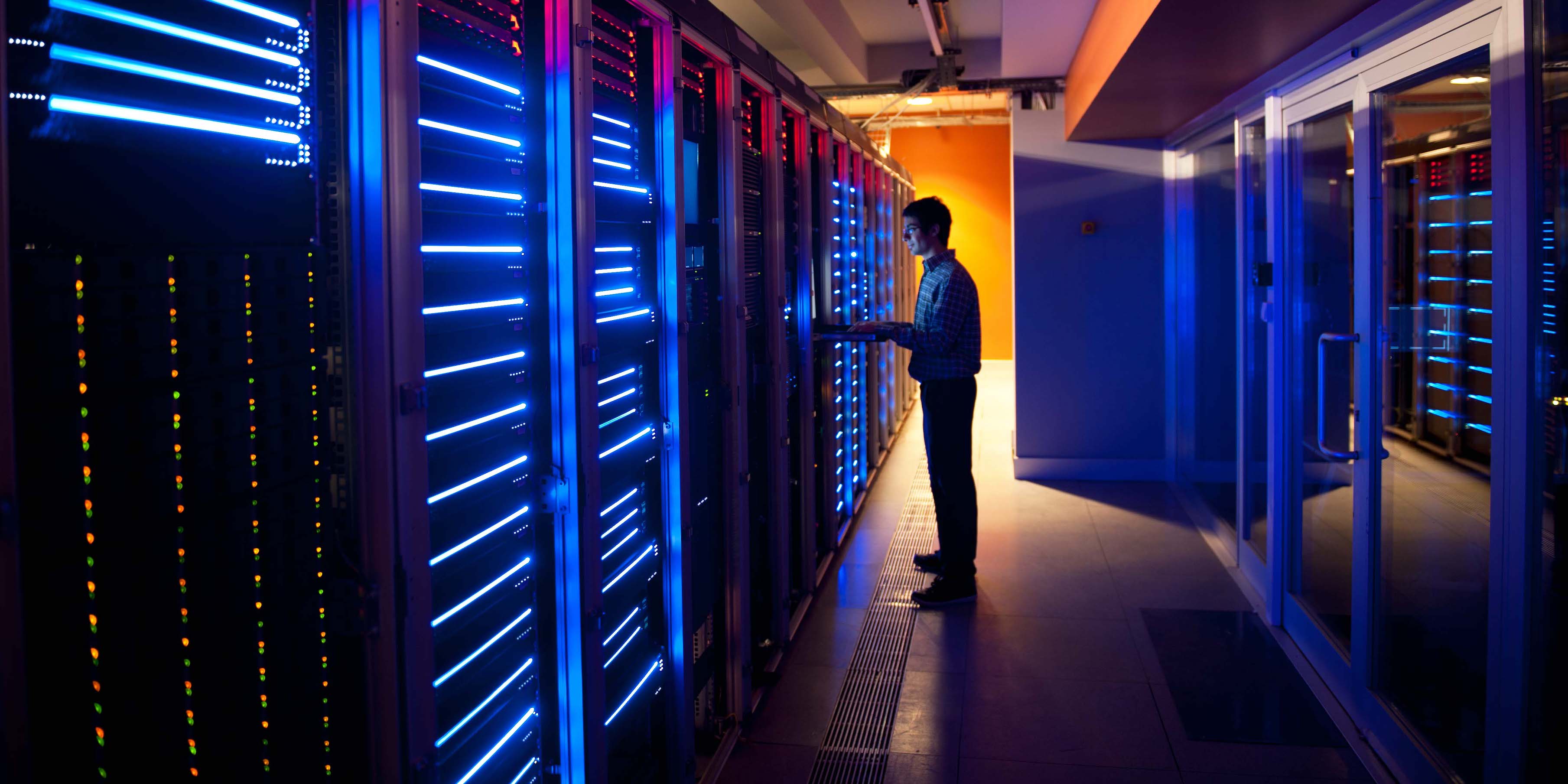 male in business attire using computer in front of server bank