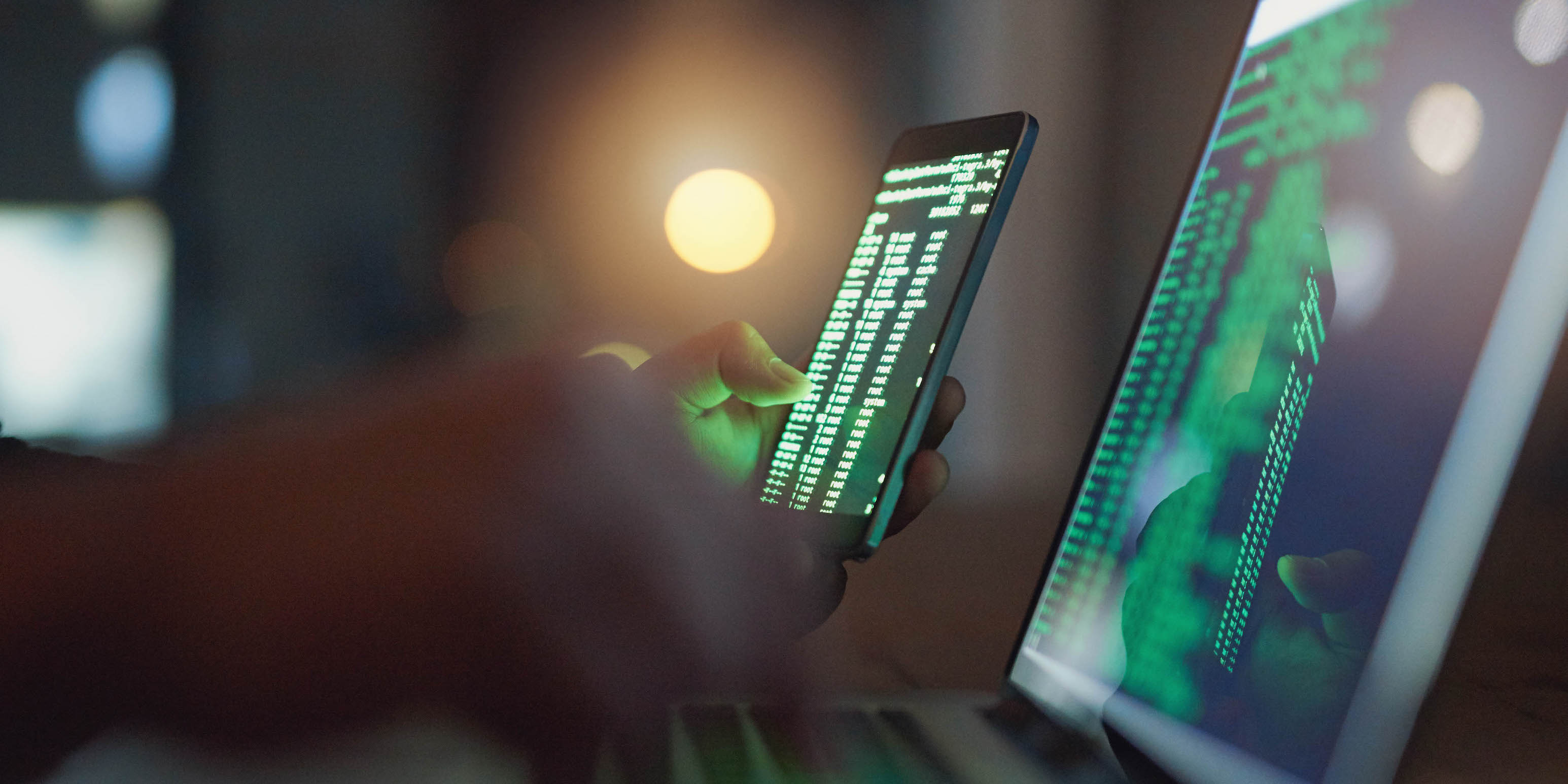 close up of hands holding cell phone and using laptop in the dark