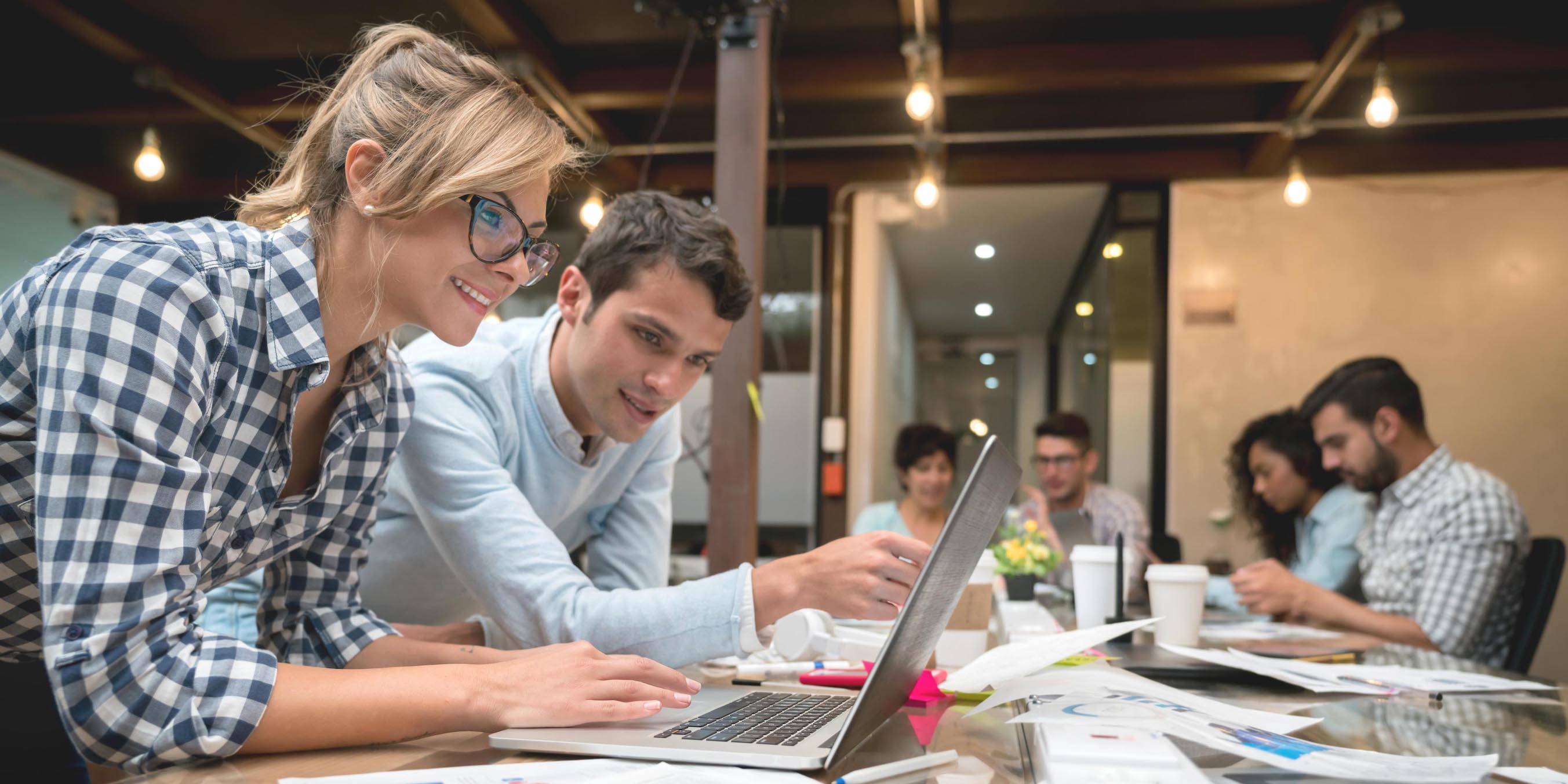 Group of people working online at a creative office using a laptop computer and smiling