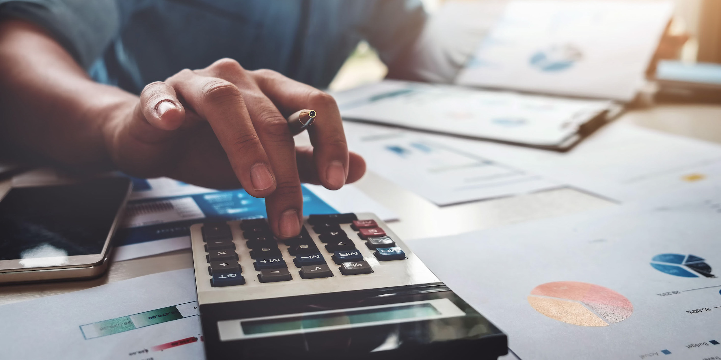 Business man using calculator with business graphs and charts in office.