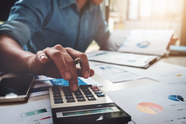 Business man using calculator with business graphs and charts in office.
