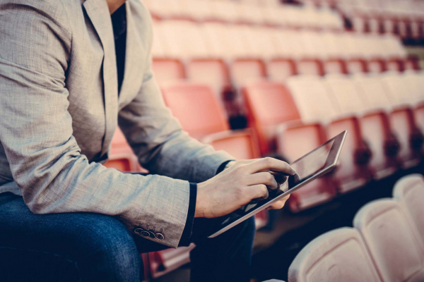 Young and successful football manager working on a tablet, and sitting on the stands alone. Cropped photo.