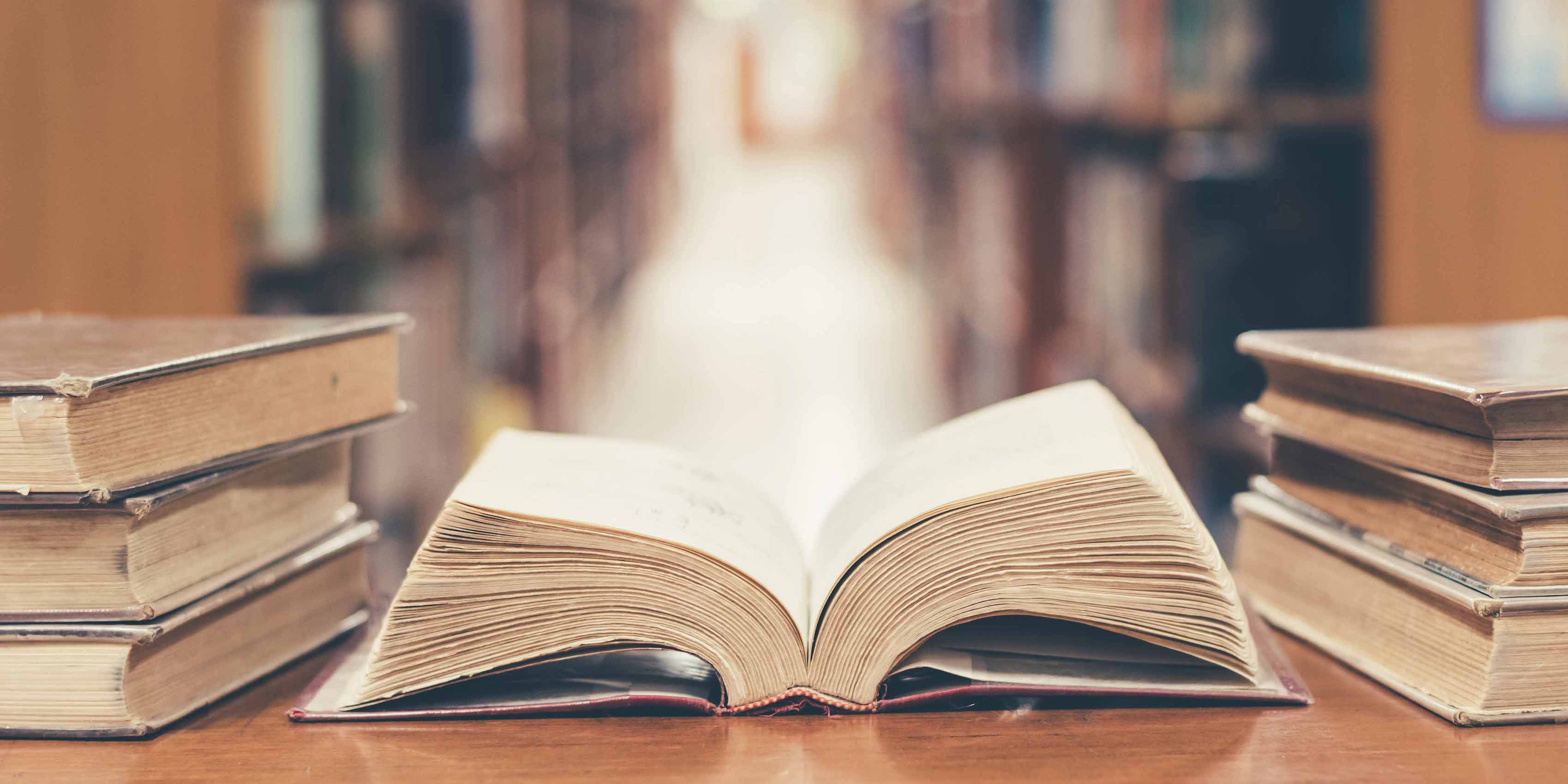 open book in library, stack piles of literature on reading desk